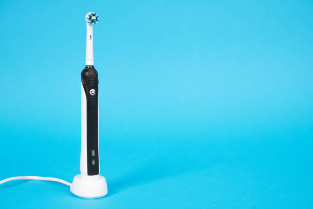 istock Electrical tooth brush of round shape with wire, setting in special stand. Studio, bright blue background, copy space for text or advertisement. 1245084698
