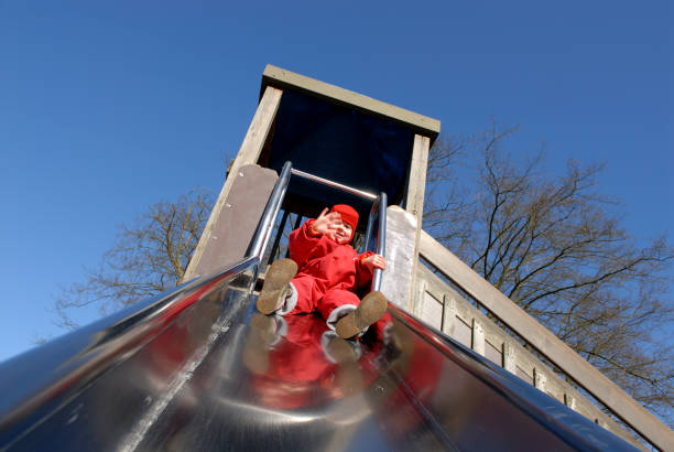 Little girl (aged 2 years) being happy on the playground slide. There is some motion blur on the waving hand.