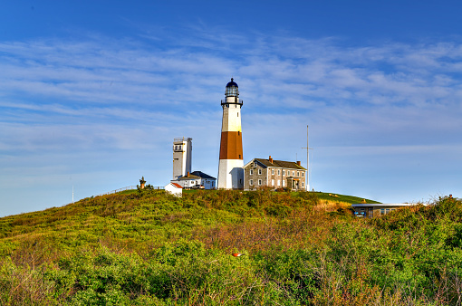 Montauk Point Lighthouse, portrait orientation.   Located in Montauk Point State Park, Montauk, Long Island, New York.  In evening sun with blue sky and clouds in the background.