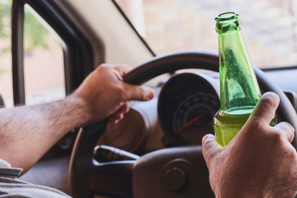 Drunk driving. Impaired Driving An unrecognizable man drinking beer while driving car. Concepts of driving under the influence, drunk driving or impaired driving pics of drunk driving accidents stock pictures, royalty-free photos & images