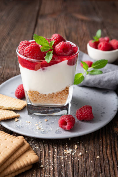 No bake cheesecake dessert in a glass jar topped with raspberry puree and fresh berries stock photo