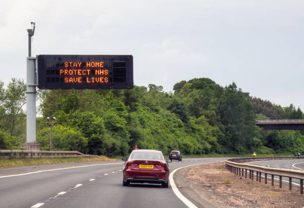 M8 Motorway, Scotland - Cars travelling towards Glasgow passing a Government sign advising people to avoid unnecessary travel during Covid-19 lockdown measures.