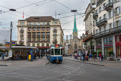 Zurich, Switzerland - October 6, 2018: People visiting the Paradeplatz square with its famous tram station, Savoy Hotel and a view to Fraumünster church. A landmark and famous tourist destination.