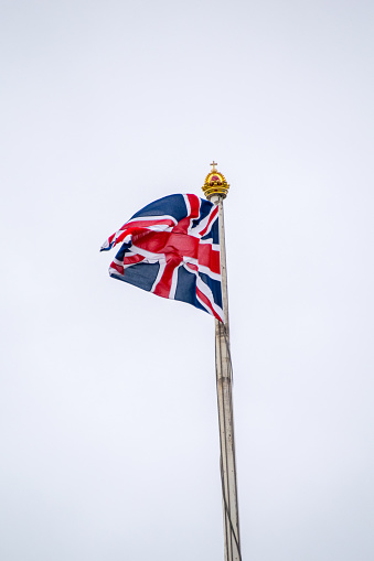 The Royal Standard of the United Kingdom waving with the UK flag with blurred Buckingham Palace in the background. 3d illustration render. rippled textile