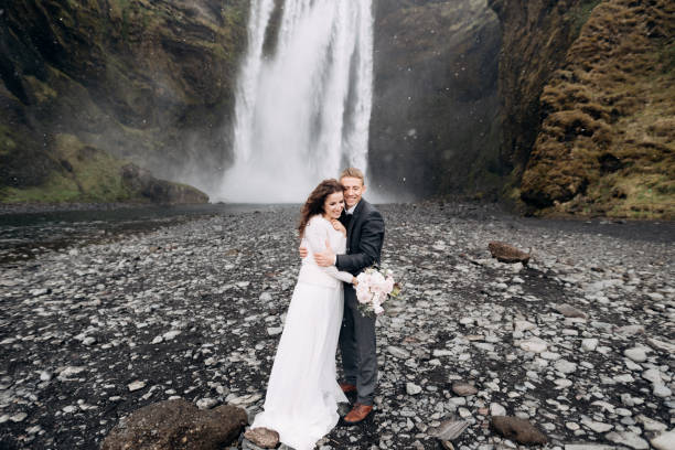 lo sposo abbraccia la sposa, nevica. coppia di nozze vicino alla cascata di skogafoss. destinazione islanda matrimonio. - elope foto e immagini stock