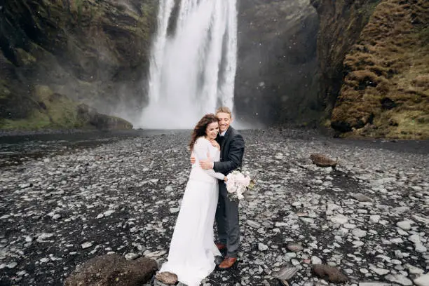 Photo of The groom hugs the bride, it is snowing. Wedding couple near Skogafoss waterfall. Destination Iceland wedding.