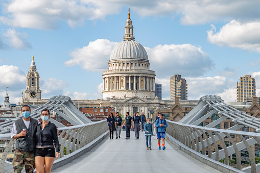 A view of St. Paul's Cathedral on The Millennium Footbridge with people wearing protective face masks.  London, England - 2 May 2020