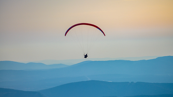 Silhouette of man paragliding above the mountains against sky during dusk.