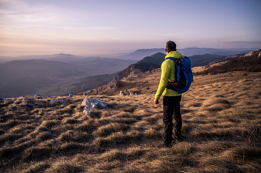 Rear view of man looking at view while standing on mountain during sunset.