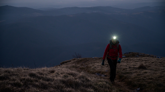 Woman wearing electric torch hiking on mountain during dusk.