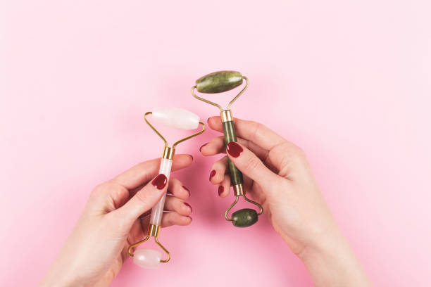 istock Two jade rollers in woman hands on pink background. 1245177294