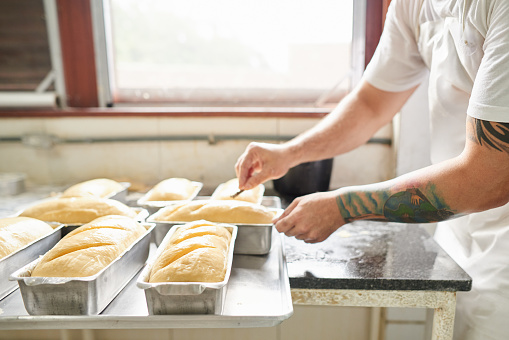 Close-up of a male baker hand scoring bread dough at bakery