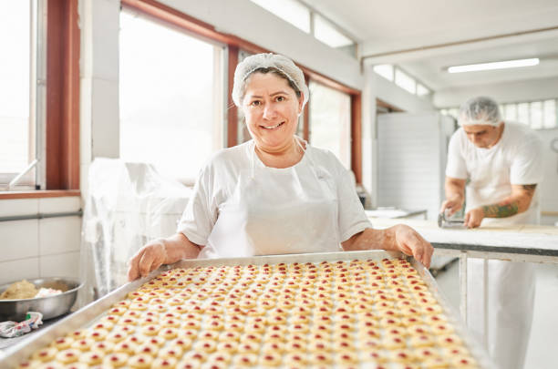 Proud female baker in bakery Portrait of a female baker holding tray with raw cookies at a bakery baker occupation stock pictures, royalty-free photos & images