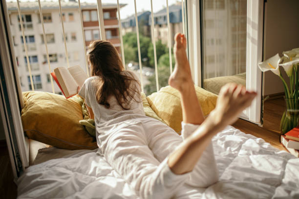 istock Young woman reading book on bed at home 1245207650