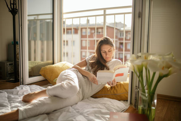 istock Young woman reading book on bed at home 1245207666