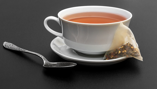 Cup of tea with tea spoon and tea bag on black.