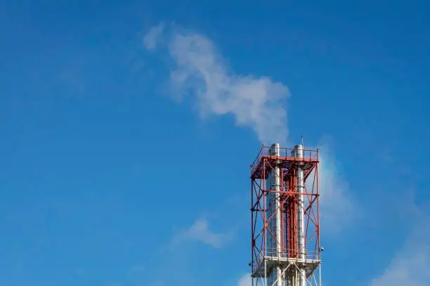 Air pollution with smoke through industrial pipes against blue sky. Multi pipe structure against blue sky on sunny day.