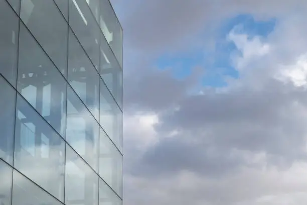 Glass wall of modern office building against cloudy sky. Copy space for text.