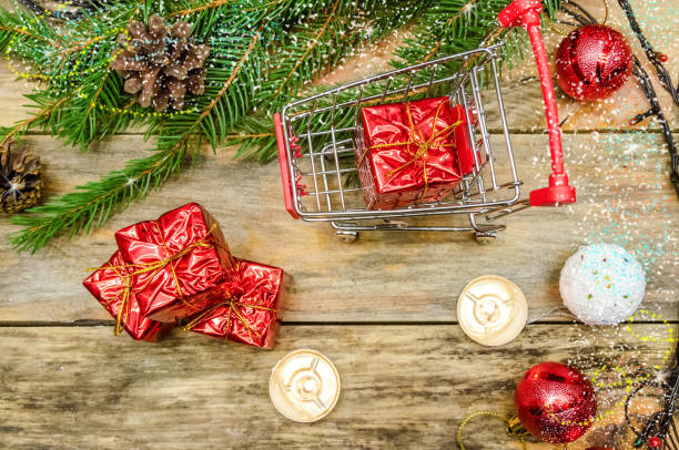 istock Mini cart with gift boxes on wooden background with Christmas tree, lighted candles, cones, Christmas tree toys. The concept of shopping for Christmas gifts. Beautiful, bright Christmas background 1245222531