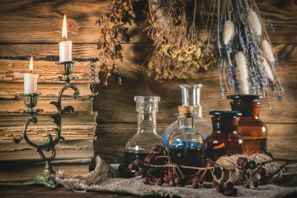 Magic potions and old books on the witch doctor table close up background.