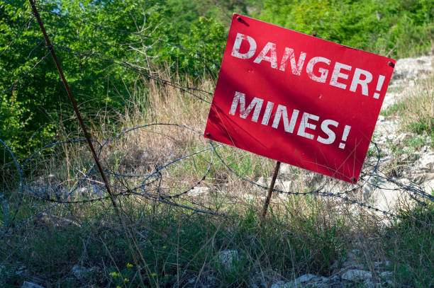 segno rosso danger mines di fronte a un campo minato recintato con filo spinato. - exploding mining bomb mine foto e immagini stock