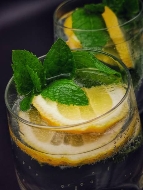 Glas of cold sparkling water with lemon and mint isolated on black background
