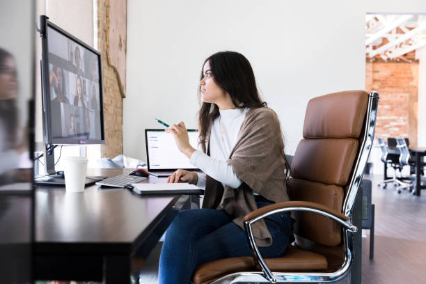 Young business owner checks with employees through video The young business owner checks in with her employees via video conferencing. office chair stock pictures, royalty-free photos & images