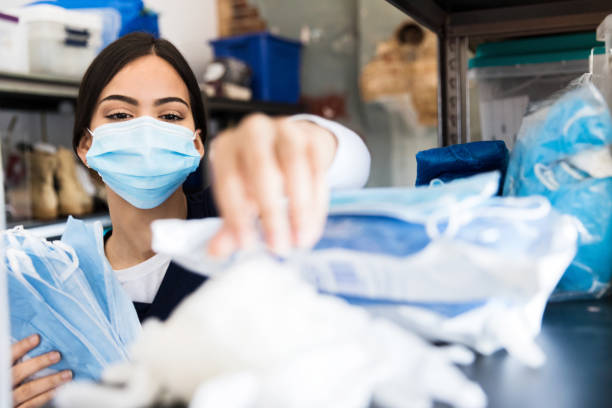 Nurse reaches for supplies in clinic supply room A confident nurse reaches for personal protective equipment as she prepares for a day of work in a hospital or medical clinic. The nurse is wearing a protective face mask. medical supplies stock pictures, royalty-free photos & images