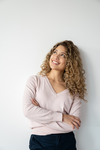 Portrait of a thoughtful young woman leaning against a white wall and smiling
