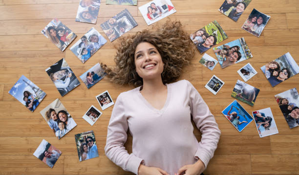 donna premurosa circondata da foto di famiglia mentre giace sul pavimento - family album foto e immagini stock