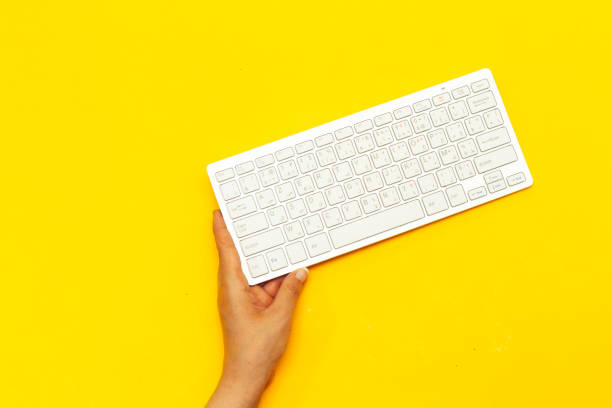 istock hand holding modern aluminum computer keyboard isolated on yellow background 1245283546