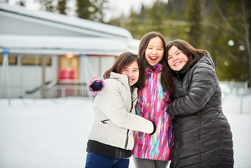 Portrait of three girls in winter wear standing in school field looking at camera and smiling