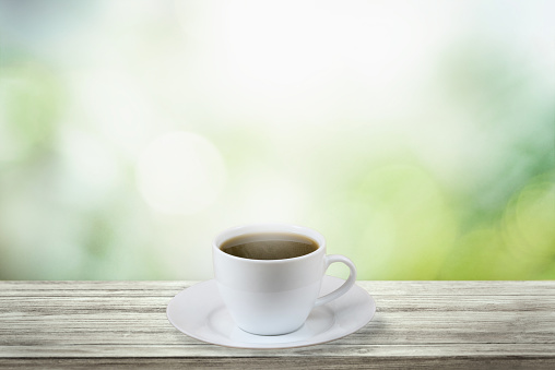 White coffee cup on wood table with nature background and glowing sparkles