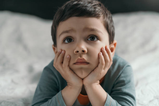istock thoughtful little boy holding hands on face and looking up while lying on bed 1245324336
