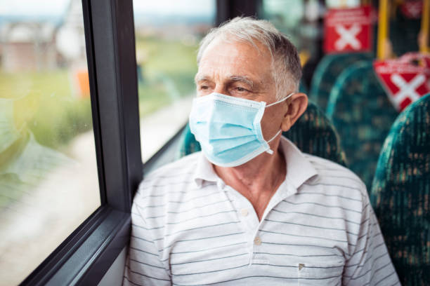 Senior man with respiratory mask traveling in the public transport by bus stock photo
