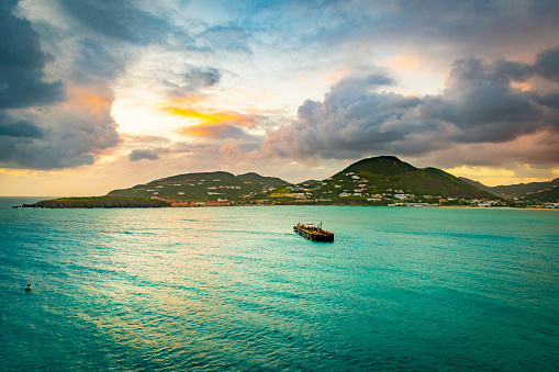 Cloudy sunset ocean view in the Caribbean with cruise ship fuel bunker vessel sailing to coast. Mountains stretch along the coastline landscape with endless water all around.