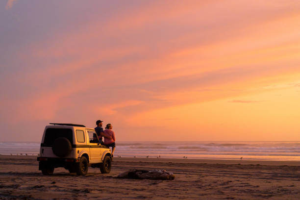 Couple get out of car to watch sunrise Orange sky illuminates Pacific Ocean in distance spectacular view stock pictures, royalty-free photos & images