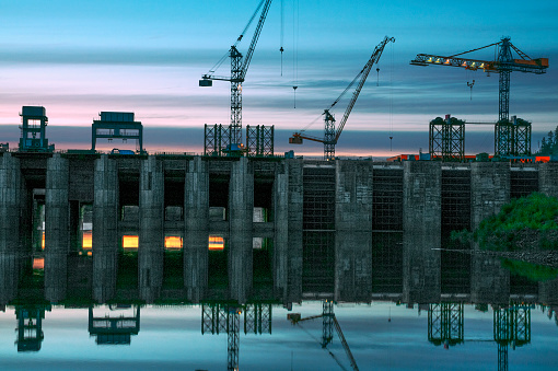 Twilight, industrial cranes, construction site, construction of a hydroelectric station on the river