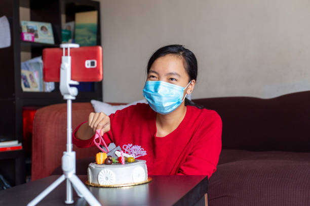 young asian girl doing teleconference birthday celebration with cake cutting ceremony asian chinese teenage female celebrating own birthday with friends virtually using online video call with smartphone virtual birthday celebration stock pictures, royalty-free photos & images