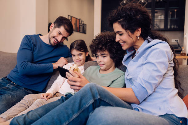 istock Young parents and their kids enjoying on the sofa and using smartphone together 1245463799