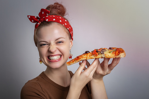 Smiling laughing young Caucasian woman girl holding eating big pizza slice. Food is joy concept
