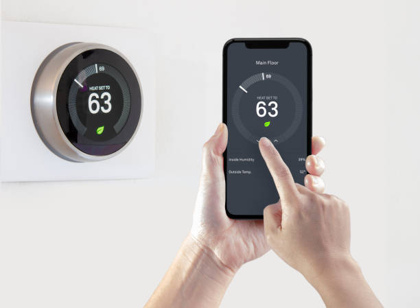 A person using a smart phone application saving energy with a wireless smart thermostat on a white background. A person using a smart phone application saving energy with a wireless smart thermostat on a white background. smart thermostat photos stock pictures, royalty-free photos & images