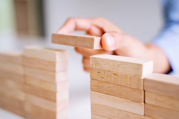 istock Close up of hand holding small wooden brick put on the wall, Risk and solution. 1245602588