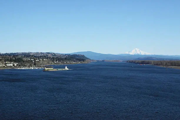 View of Columbia River under a big blue sky with Mt. Hood in the distance. A barge carrying grain from Central Washington/Oregon to be exported. Vancouver, Washington on the left and Portland, Oregon on the right.
