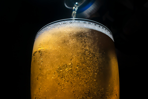 Cold beer served from a can in a glass, in a dark environment, or black background, sparkling beer concept or cold alcoholic drink.