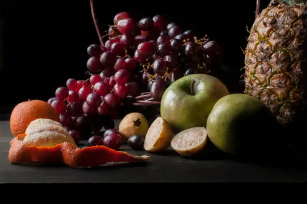 Renaissance photography or chiaroscuro style of still life fruits photography with grapes, pineapple, green apples, guavas, tangerines, and red grapes. oil painting style