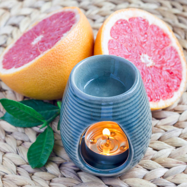 Aroma lamp with grapefruit essential oil on woven mat, grapefruits on background, square