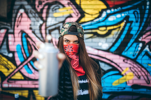 Young woman with bandana is holding aerosol can of spray paint.