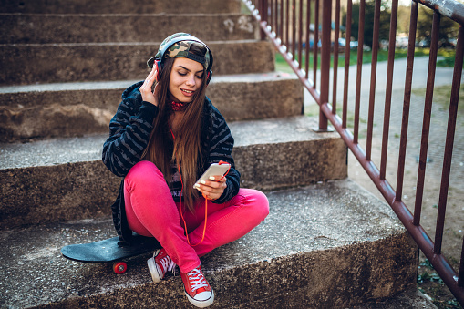Urban caucasian beautiful girl listening to music on small bleachers alone.