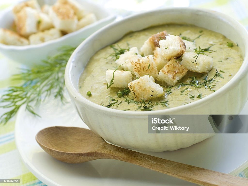White bowl of soup with croutons next to a wooden spoon A bowl of green vegetable soup with croutons and dill Squash Soup Stock Photo